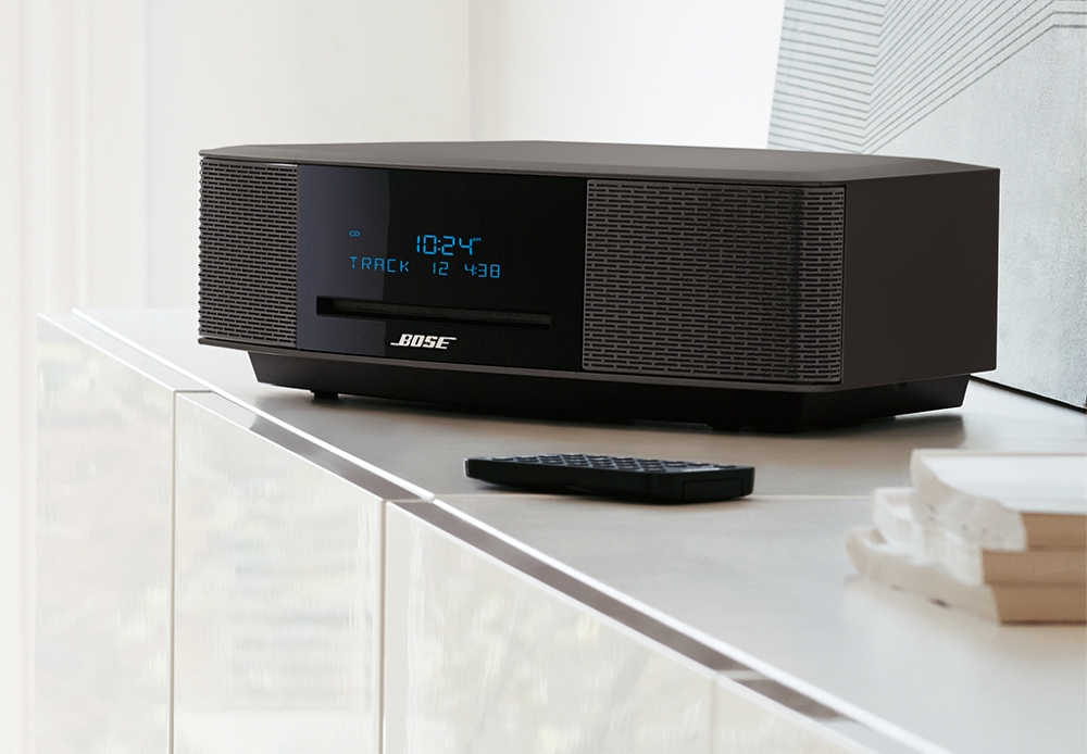 Bose Wave on a media console with remote lying next to it and digital screen on the front illuminated with the time.